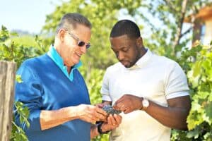 Jayson Pahlmeyer and Dwyane Wade inspecting a cluster of grapes together.